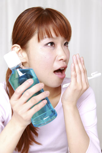 female checking her breath while holding toothbrush and a container of mouthwash