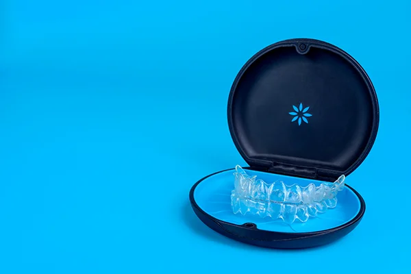 Set of clear aligners resting in an Invisalign branded case on a blue background