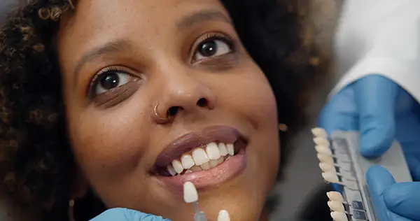 Happy female patient undergoing a dental veneer consultation, with a dentist using a shade guide to determine the perfect match.