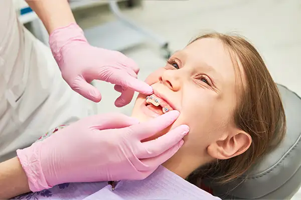 A dentist adjusting braces during a maintenance check for a young girl, emphasizing orthodontic treatment for kids.